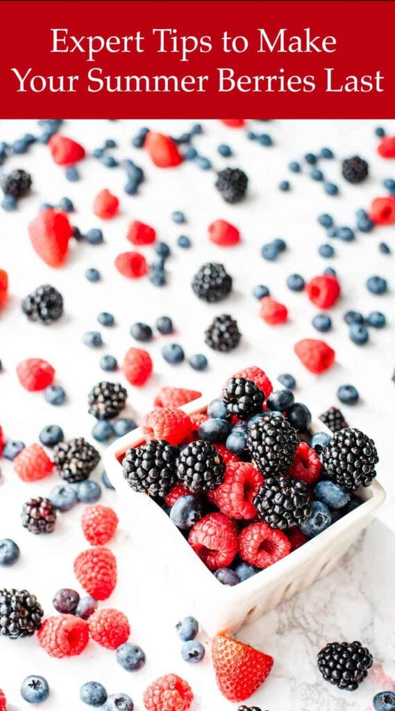 A variety of fresh summer berries are scattered on a white surface with some in a square white container. A red banner at the top of the image reads, "Expert Tips to Make Your Summer Berries Last.