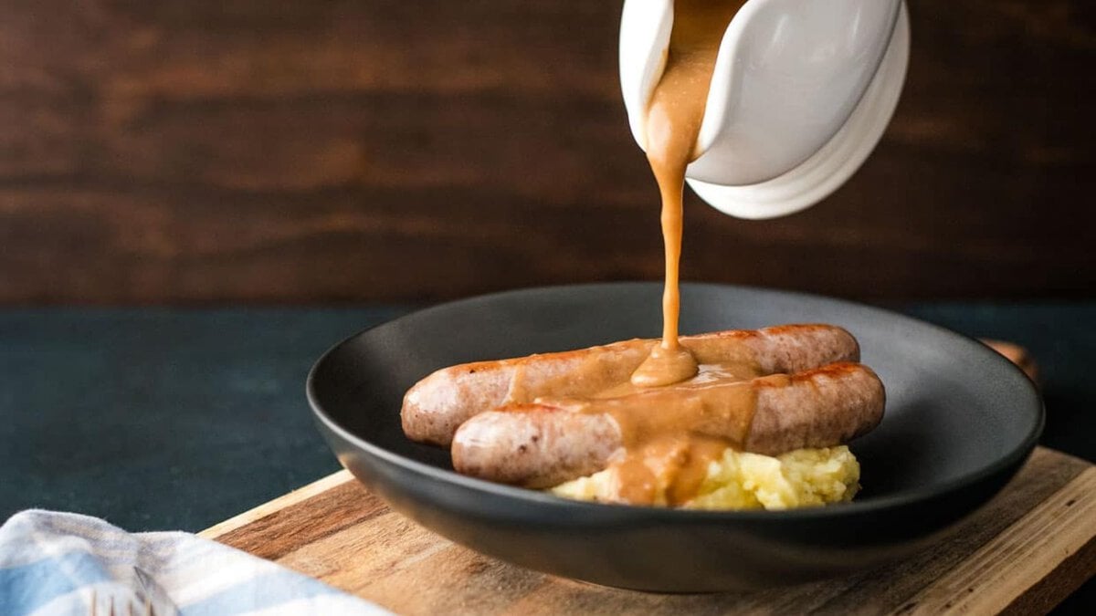Gravy being poured over sausages and mashed potatoes.