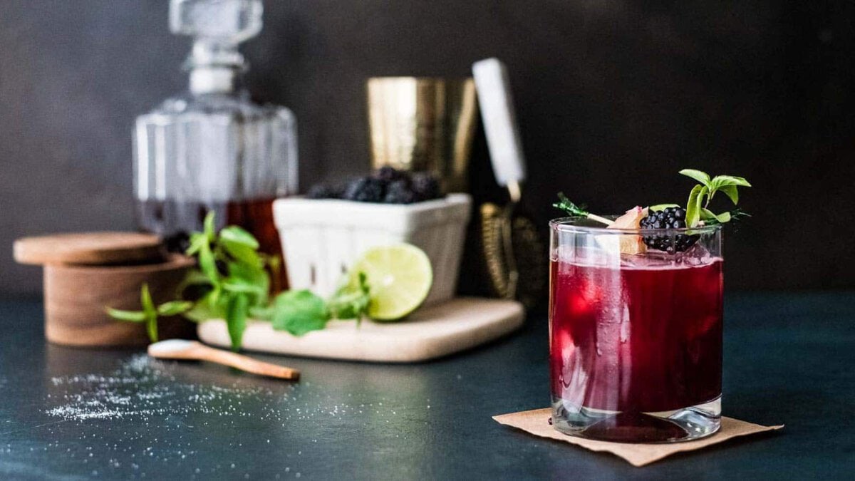 A blackberry bourbon smash in front of a cocktail bar set up.