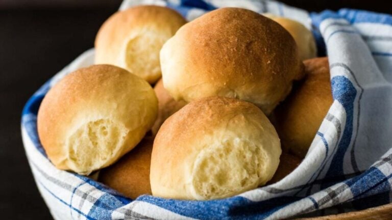 A basket of golden brown dinner rolls lined with a blue and white checkered cloth.