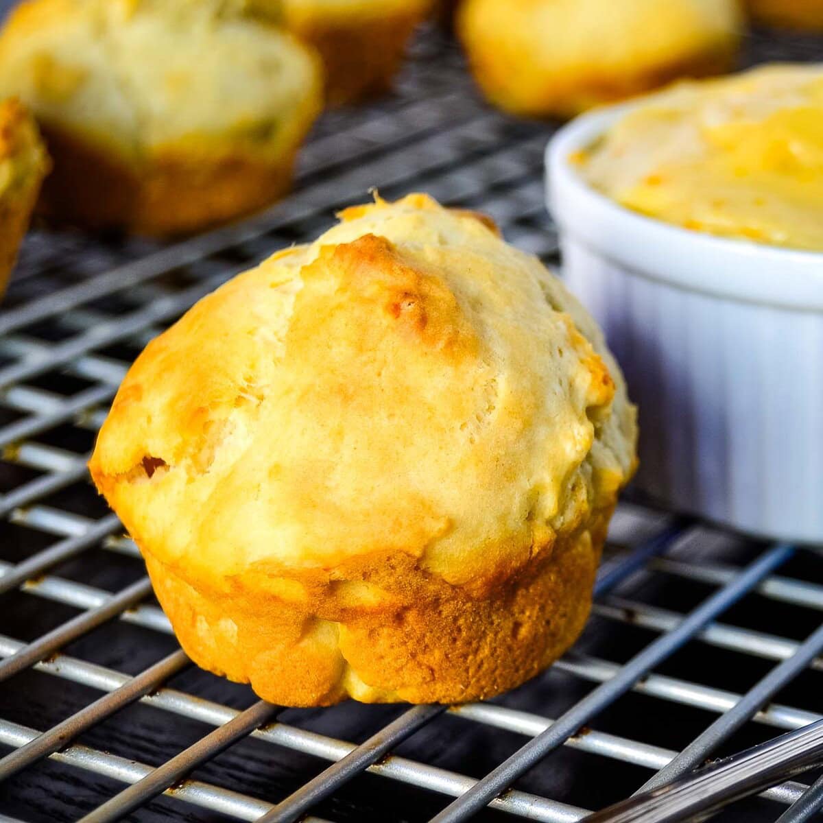 A freshly baked buttermilk drop biscuit cooling on a wire rack with other biscuits and a white ramekin in the background.