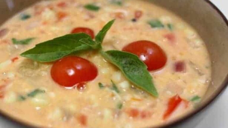 A bowl of corn and tomato soup with fresh basil.