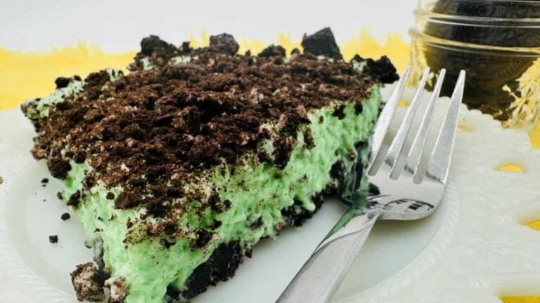 Slice of mint chocolate chip ice cream pie with crushed cookies on top, served on a white plate with a fork.