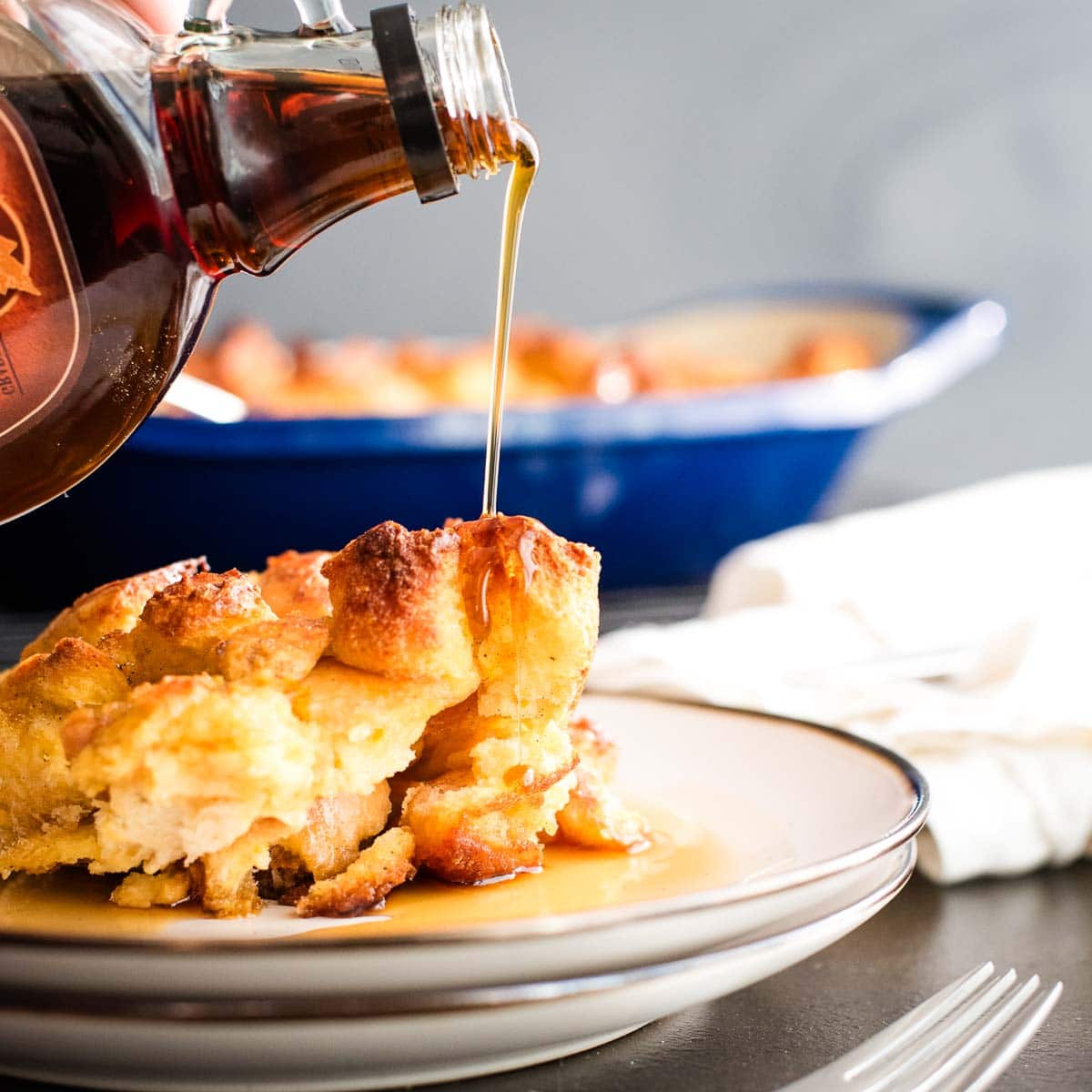 A serving of french toast on a plate with maple syrup being poured over the top.