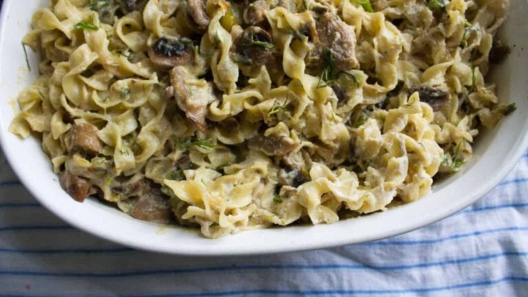 A bowl of creamy pasta with mushrooms and herbs, placed on a blue-striped cloth.