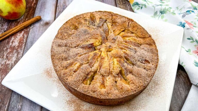 An apple cake on a white plate with cinnamon sticks.