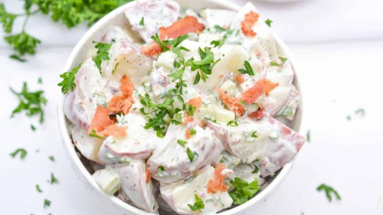 Red potato salad in bowl with bacon and parsley garnish.