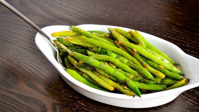 Screaming skillet green beans in a white bowl on a wooden table.