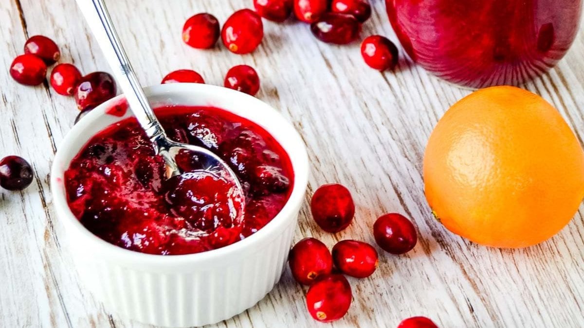 Small jar of clementine cranberry jam with fresh fruit nearby.