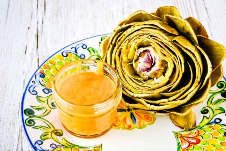 Steamed artichoke halves served alongside a vibrant spicy mango dipping sauce, presented on a simple background to highlight the bright sauce and tender artichoke texture.