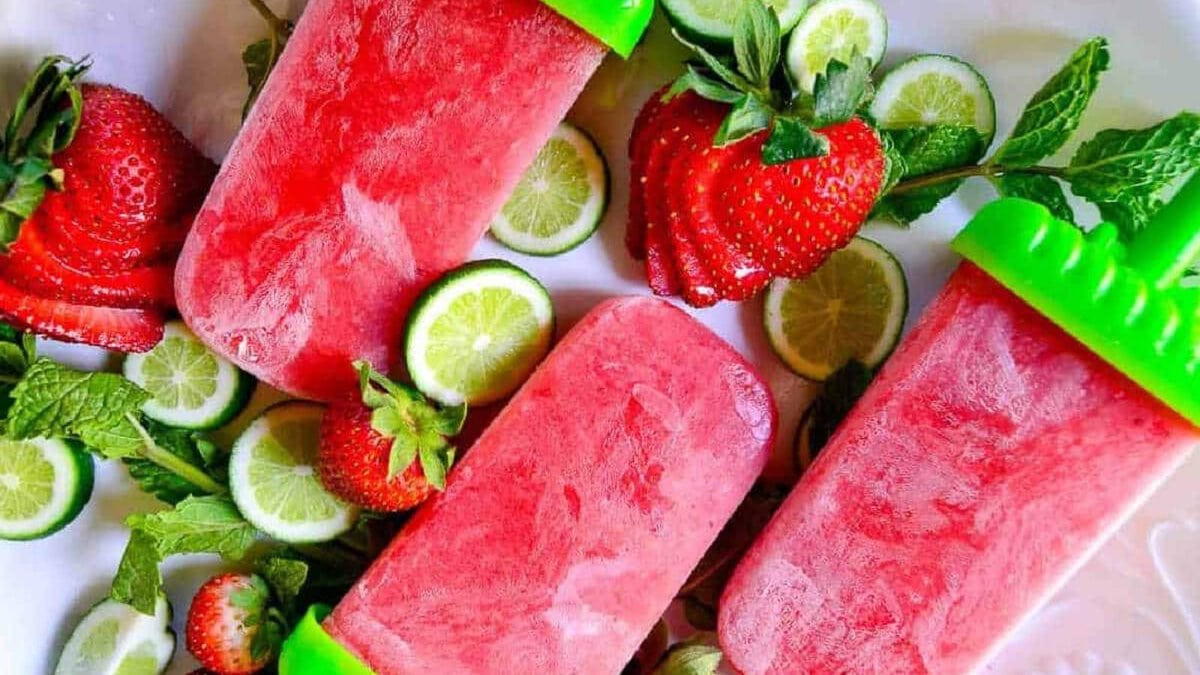 Strawberry mojito wine popsicles on a white plate with strawberries lime and mint leaves.