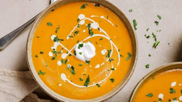 Two bowls of sweet potato and red pepper soup with sour cream and parsley.