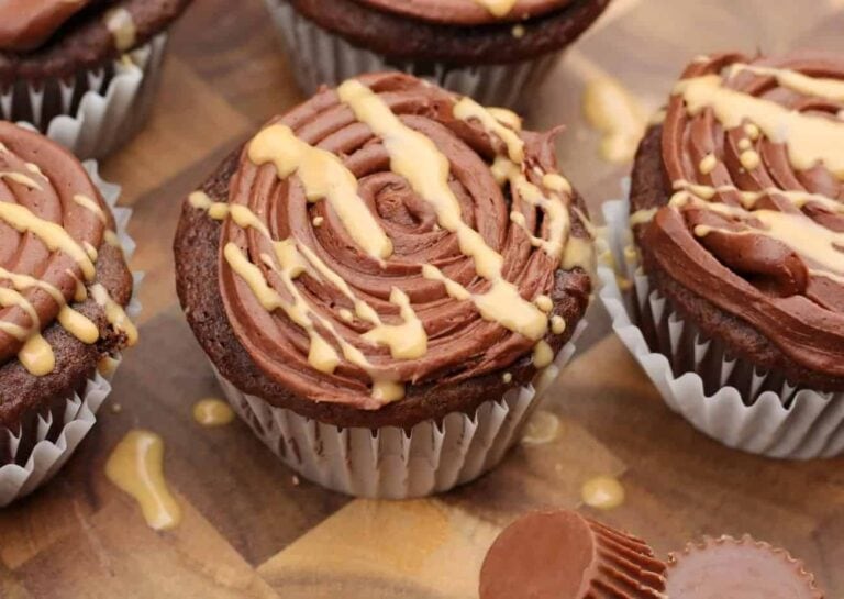 Sweet treats of chocolate cupcakes topped with swirled chocolate frosting and drizzled with peanut butter sit invitingly on a wooden surface, just like Grandma's kitchen magic.