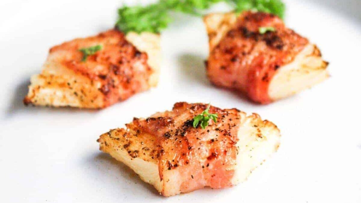 Bacon wrapped pineapple on a white plate.