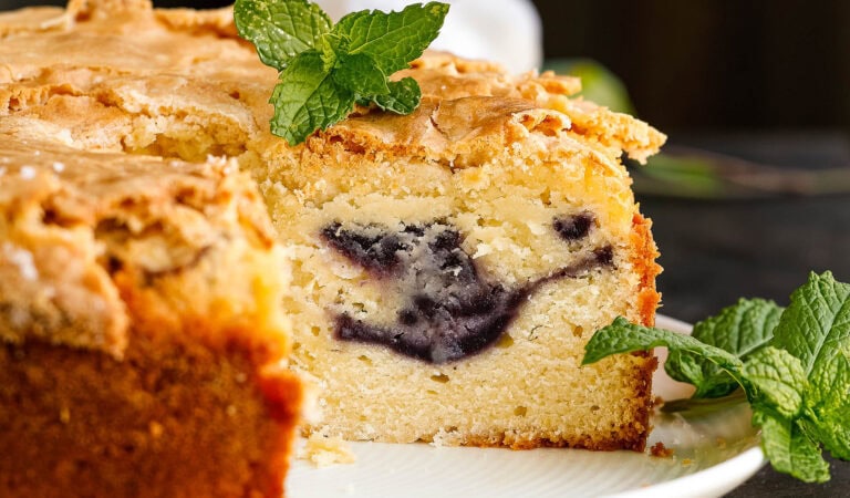 A close-up of a sliced pound cake with a blueberry swirl in the center, garnished with fresh mint leaves on top and on the plate.