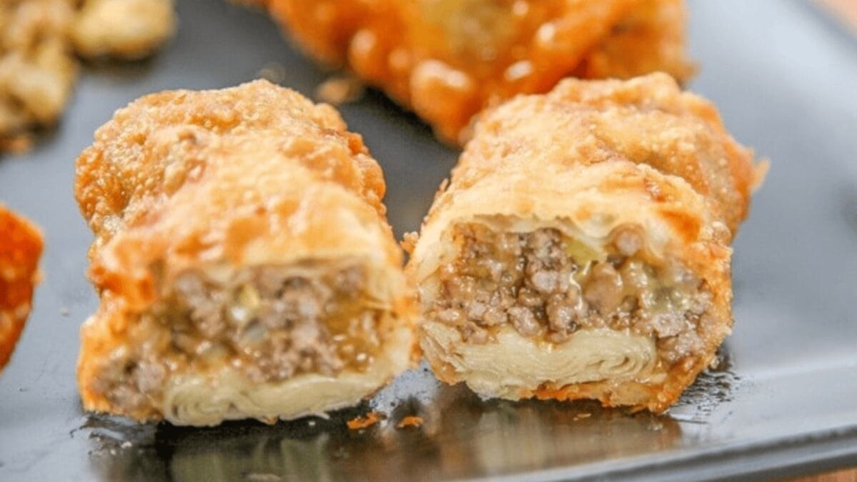 A cut open egg roll showing cheese, hamburger meat, and pickles.