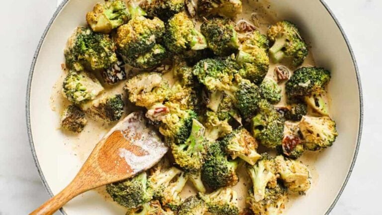 A skillet filled with cooked broccoli florets in a creamy sauce, with a wooden spoon resting inside.