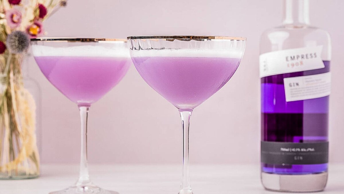 Two empress 1908 gin sours next to a bottle of purple gin.