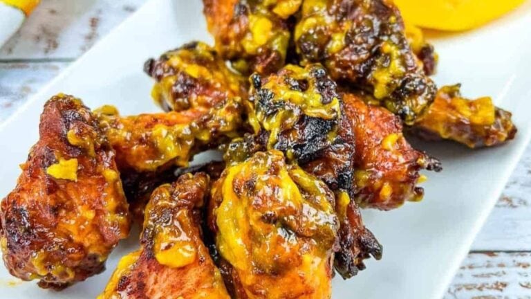 Plate of cooked chicken wings coated in a yellow and brown sauce, served on a white rectangular dish—perfect party snacks or appetizers for any gathering.