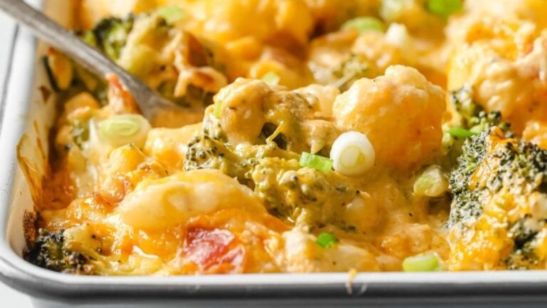 A close-up of a baked casserole with broccoli, cauliflower, cheese, and green onions in a baking dish.