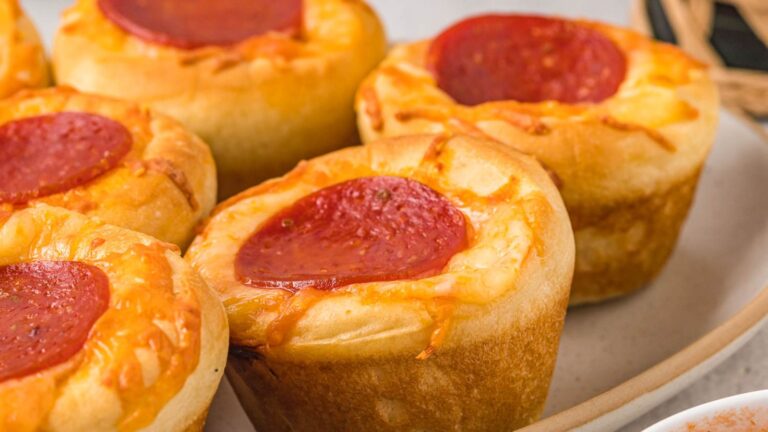 Several pepperoni pizza muffins topped with melted cheese and a slice of pepperoni are arranged on a white plate.