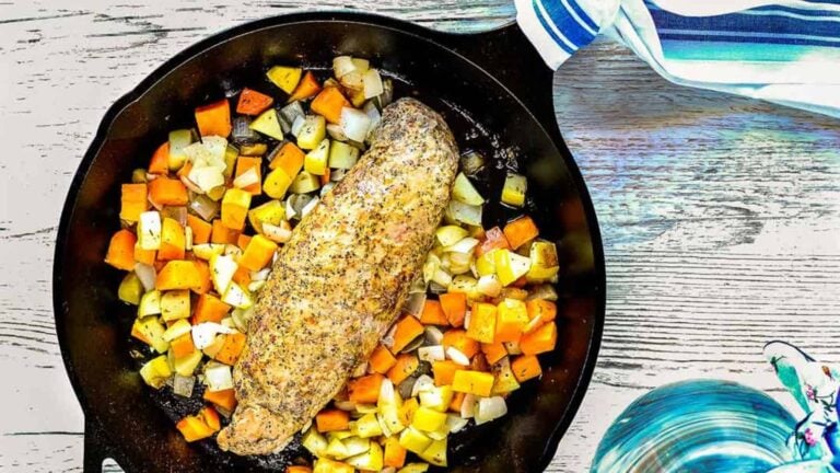 Cooked seasoned pork surrounded by diced vegetables in a black skillet on a wooden table.
