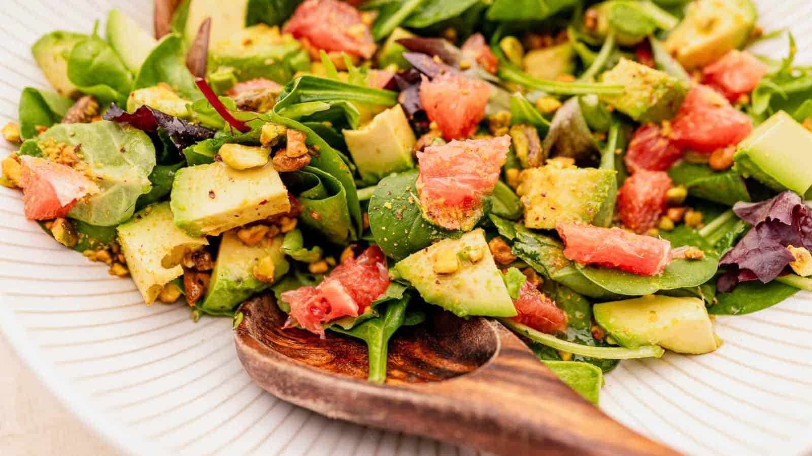 A plate of mixed green salad with avocado, grapefruit segments, and chopped nuts, served with a wooden spoon—an easy addition to healthy snacks for kids.
