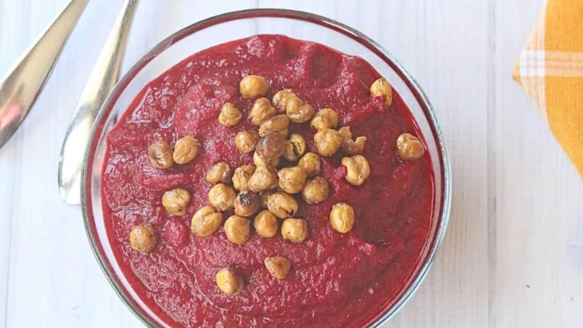 two glass bowls filled with healthy beet soup and topped with chickpeas. Two spoons beside the first bowl and a yellow napkin.