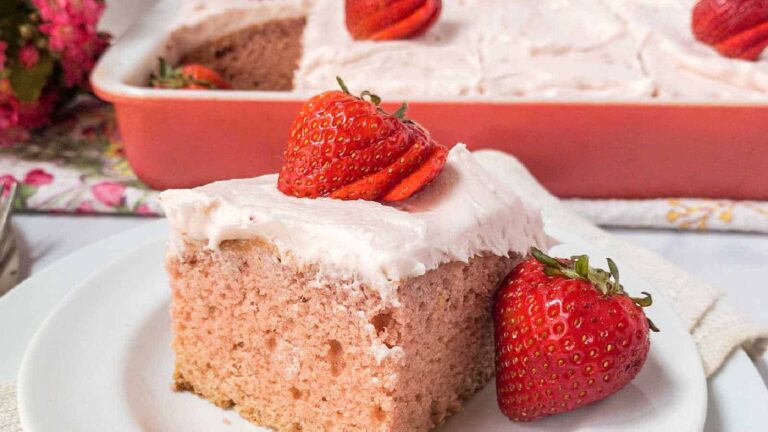 A slice of homemade strawberry cake with icing and strawberry on top.