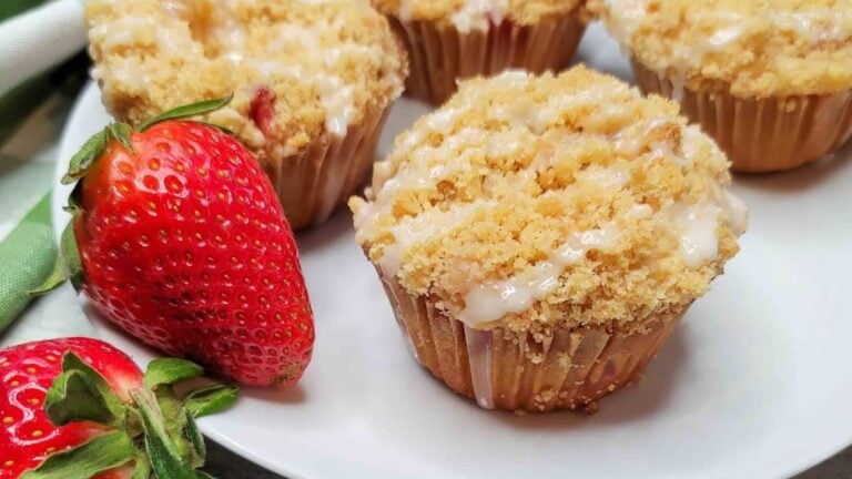 Strawberry streusel muffins on a white plate with strawberries.