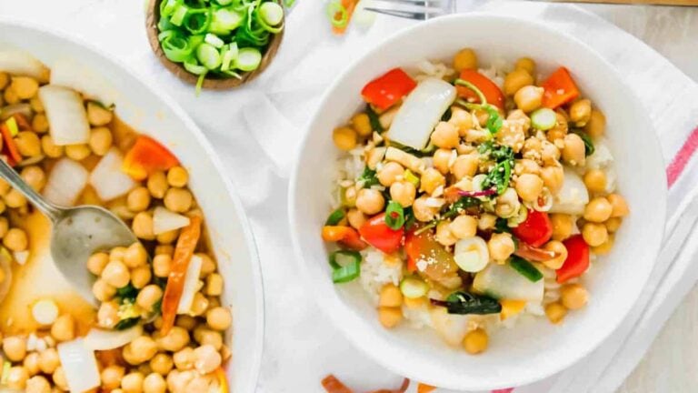 Kung pao chickpea dish in a bowl with rice and skillet off to the left.