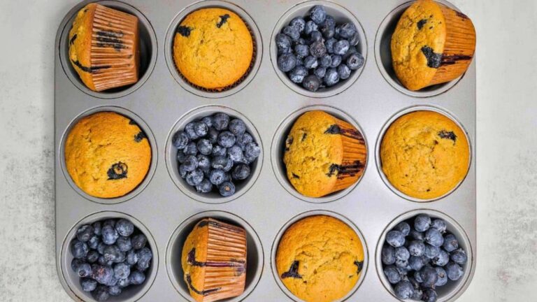 A muffin tin with six baked blueberry muffins and six cups filled with fresh blueberries, arranged alternately.