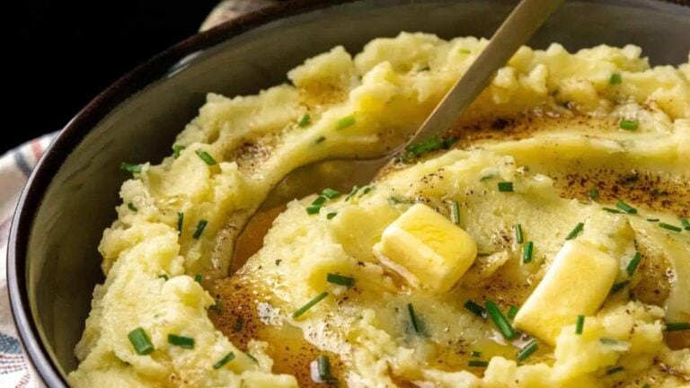 A bowl of mashed potatoes with melted butter, chopped chives, and a spoon.