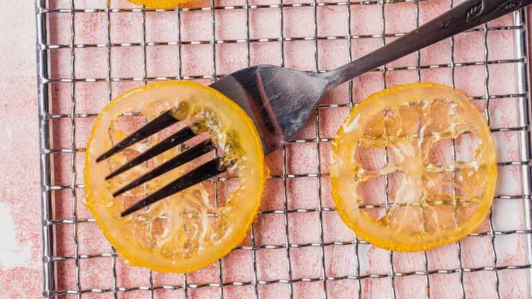Slices of candied lemon on a metal cooling rack, with a fork placed over one slice.