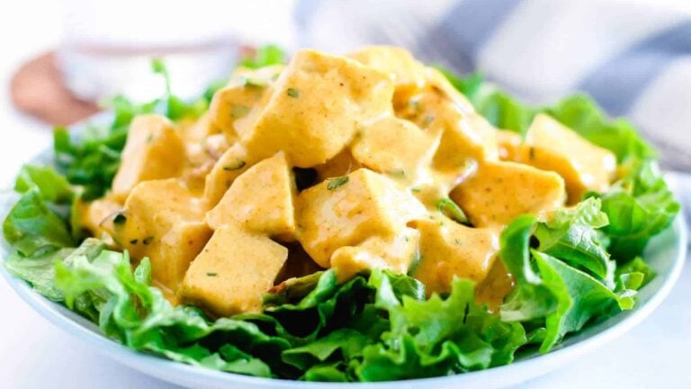 A bowl of chicken salad with cubed chicken coated in yellow curry dressing, served on a bed of fresh green lettuce leaves.