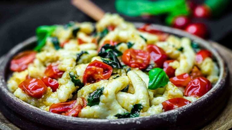 A bowl filled with pasta, topped with cherry tomatoes and fresh basil leaves, set on a wooden surface.