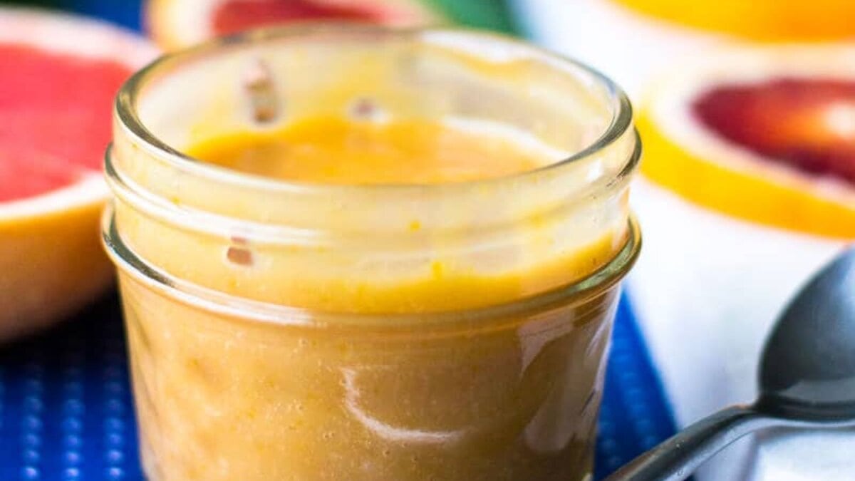 A jar of grapefruit blood orange curd with grapefruit slices and a spoon.