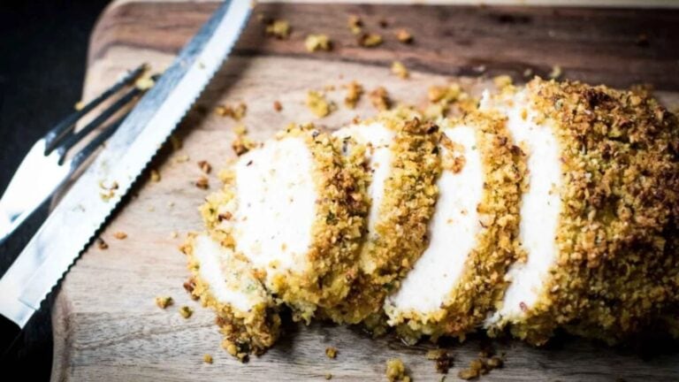 Sliced breaded chicken on a wooden cutting board next to a serrated knife.