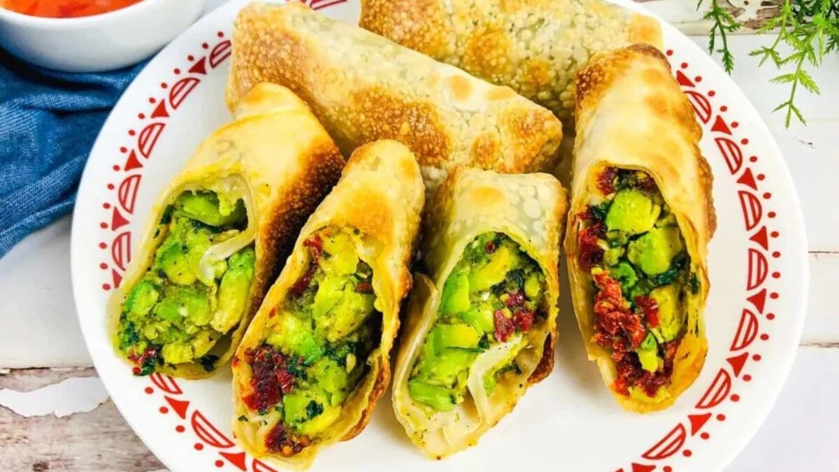 White plate with several avocado egg rolls, cut open to see the inside avocado