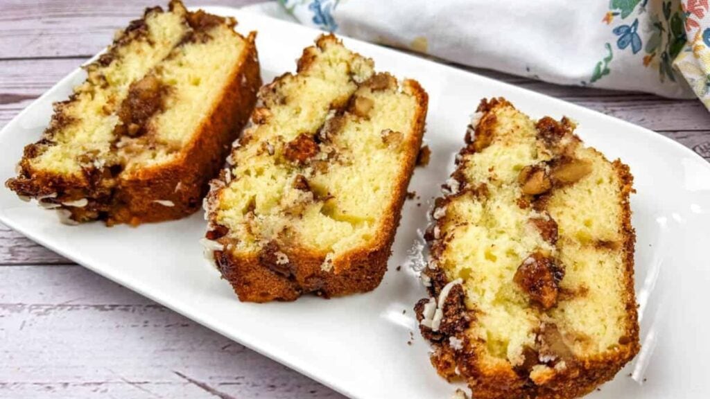 Three slices of cake with a crumbly cinnamon and nut filling are arranged on a white rectangular plate.
