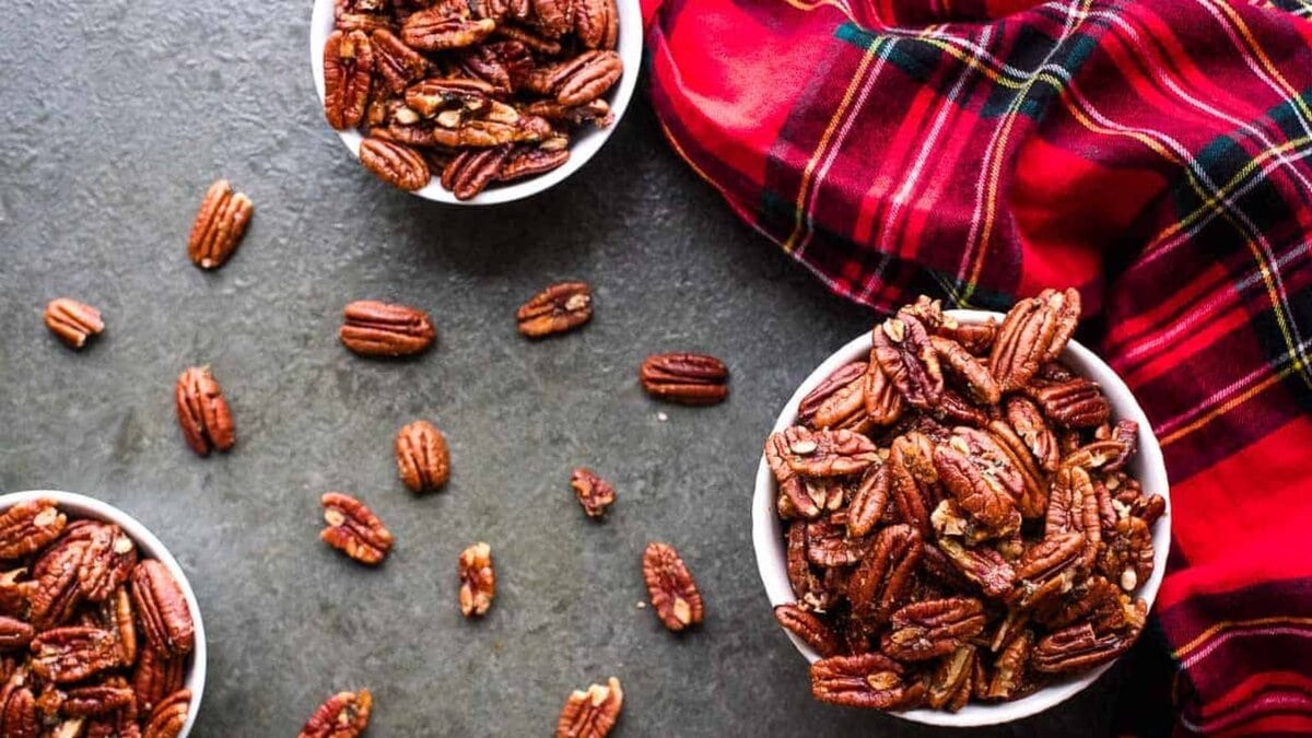 Three bowls of brown butter roasted pecans on a gray background next to a red tartan cloth.