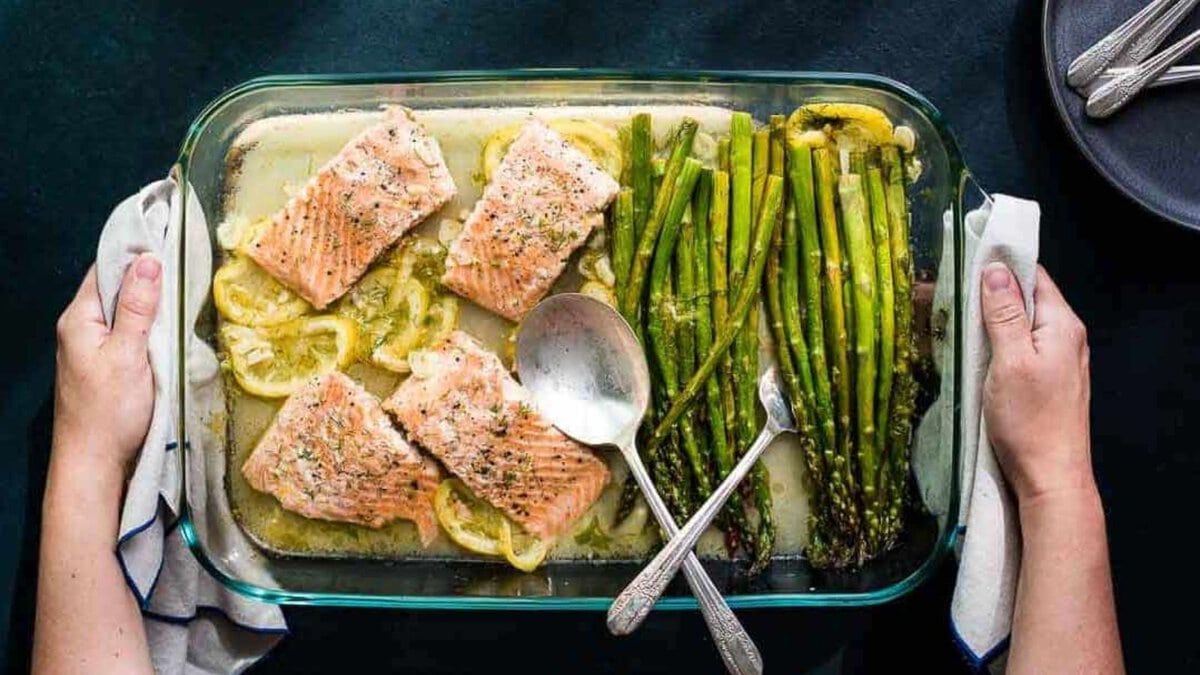 Hands holding a baking dish with Lemon Dill Salmon and Asparagus.