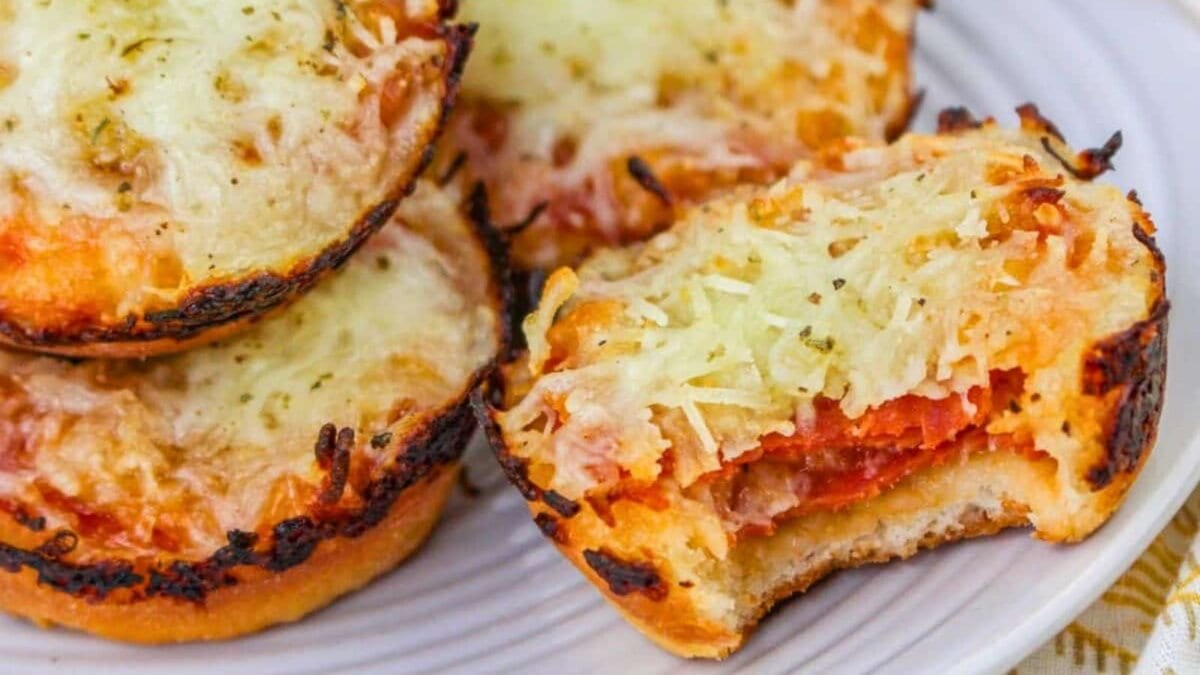 Mini pizzas with melted cheese and tomato sauce on a plate, one with a bite taken out.
