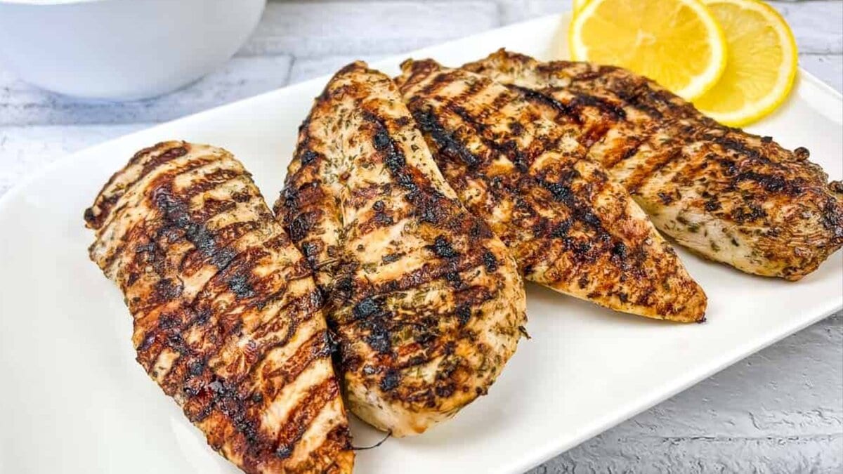 Grilled Greek Chicken on a white plate with lemon slices.