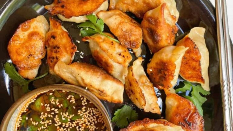 Crispy-bottom pan-fried dumplings with juicy and savory fillings on a black plate with a sauce on the side.
