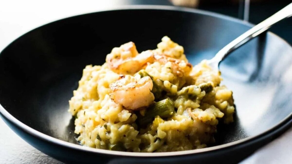 Shrimp asparagus risotto in a dark bowl on a blue background with a napkin and glass of wine.