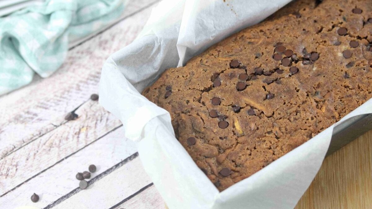 Chocolate protein zucchini in a loaf pan lined with parchment paper and chocolate chips around it.