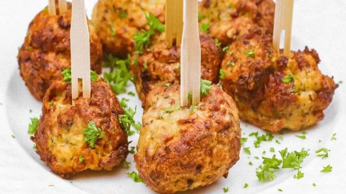 A white plate with several air-fried chicken meatballs garnished with parsley and wooden picks.