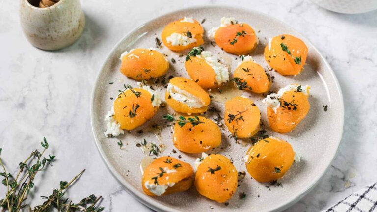 A plate of dried apricots stuffed with white cheese and sprinkled with herbs, displayed on a light-colored surface.