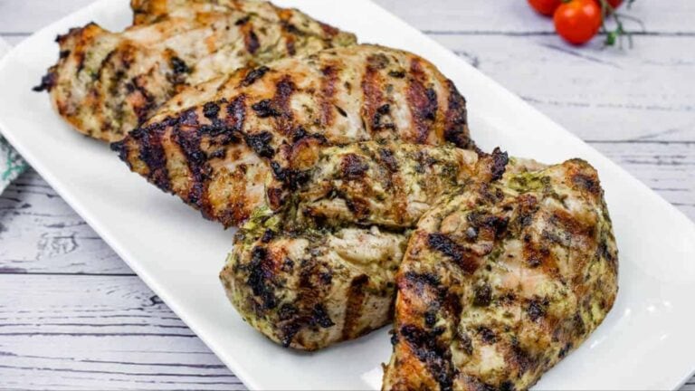 Grilled lime-garlic chicken breasts with visible char marks on a white rectangular plate, with vine tomatoes in the background.
